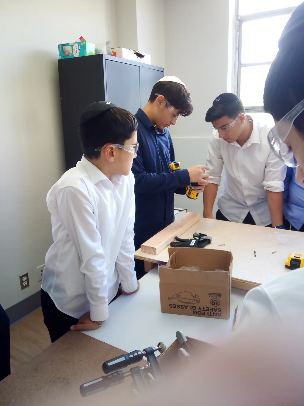 Talmidim wearing safety glasses collaborate on a woodworking project